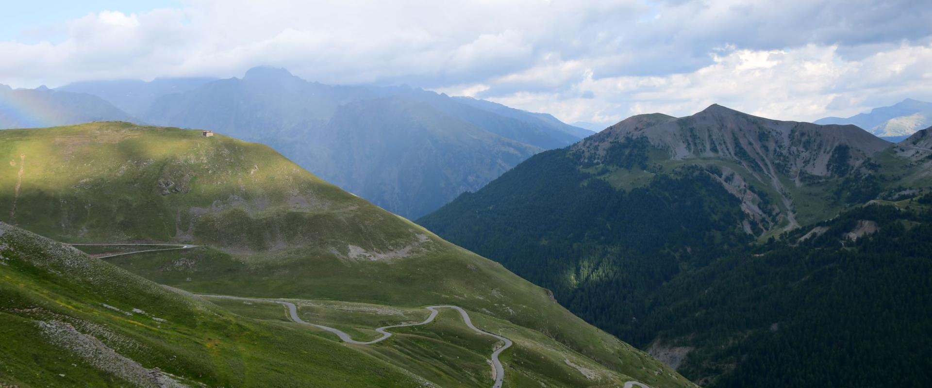 Berglandschaft mit einer gewundenen Passstraße, die sich durch grüne Hügel schlängelt, unter einem teilweise bewölkten Himmel