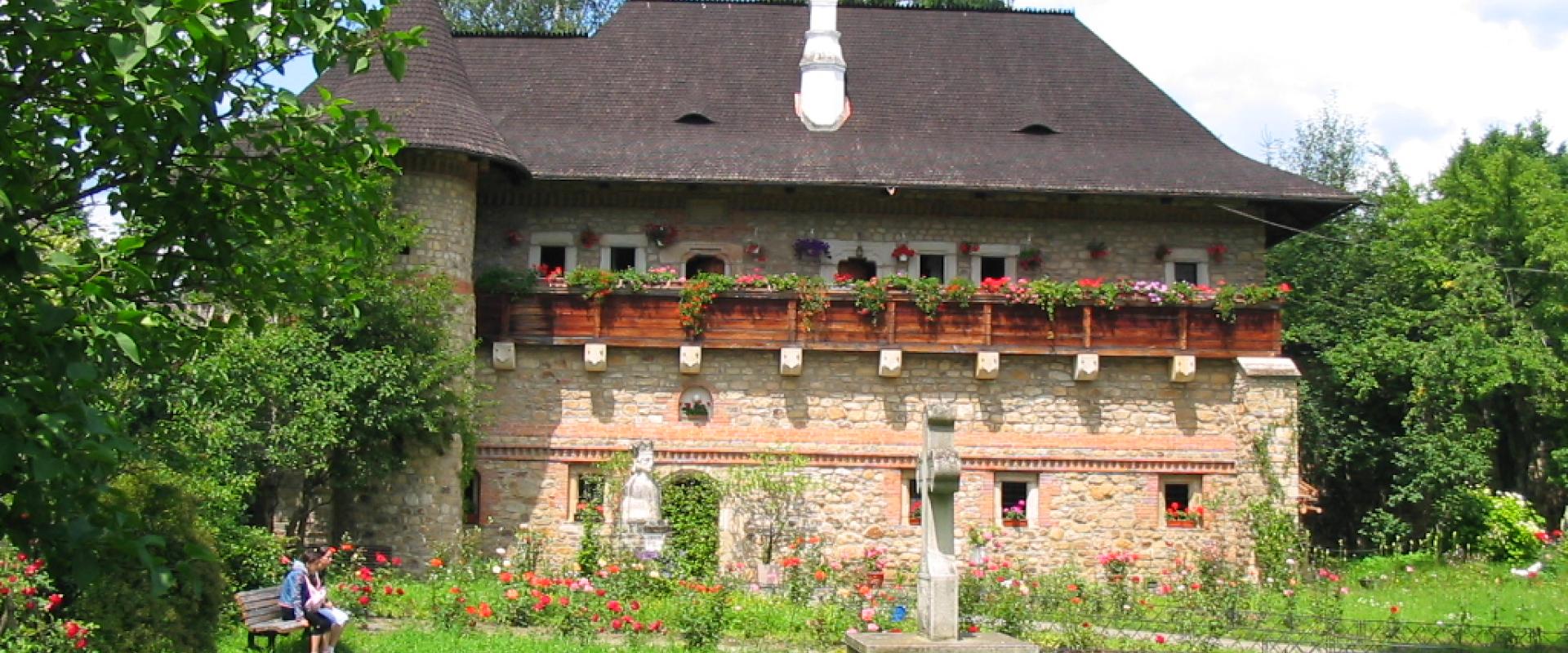 Ein traditionelles Steinhaus mit strohgedecktem Dach, farbenfrohen Blumenkästen, umgeben von einem gepflegten Garten mit Besuchern