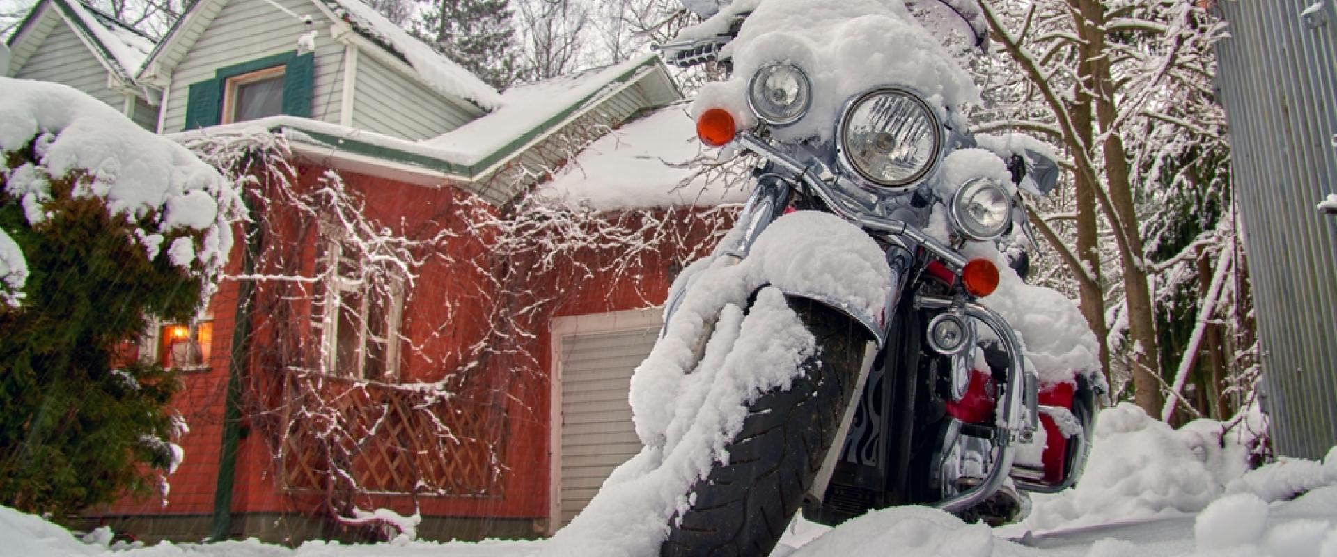 Schneebedecktes Motorrad steht vor rot weißem Haus