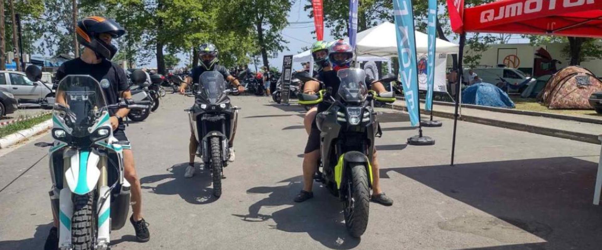 3 Motorräder auf einer Straße, am Straßenrand stehen roter und weißer Pavillon und Aufsteller 