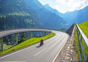 Motorradfahrer auf einer Kehre des Hochtannbergpasses, mit Berglandschaft im Hintergrund