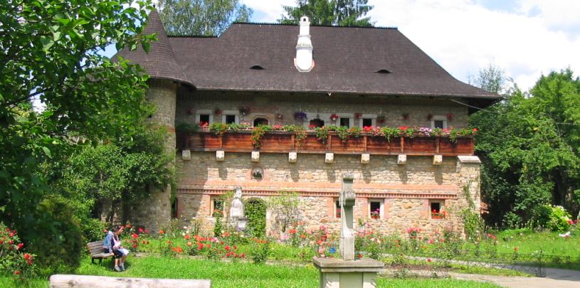 Ein traditionelles Steinhaus mit strohgedecktem Dach, farbenfrohen Blumenkästen, umgeben von einem gepflegten Garten mit Besuchern