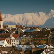 Altstadt von Sibiu mit traditionellen Gebäuden und Kirchturm, im Hintergrund die schneebedeckten Gipfel der Karpaten