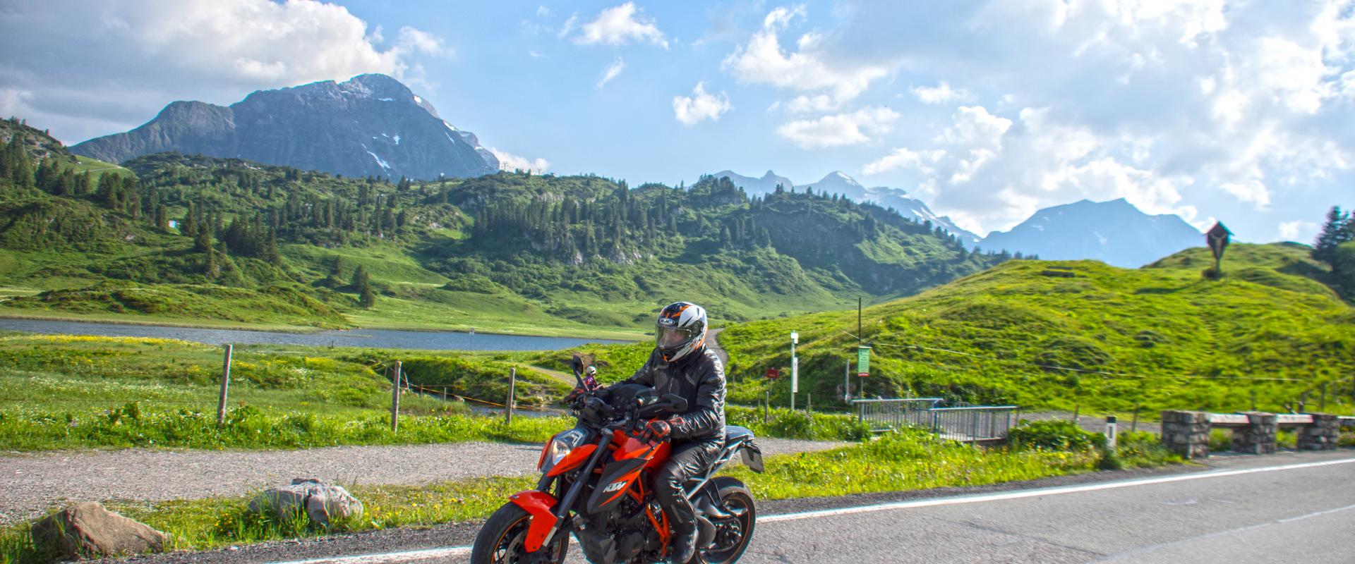 Motorradfahrer auf dem Hochtannbergpass, mit See, grünen Wiesen und Bergen im Hintergrund
