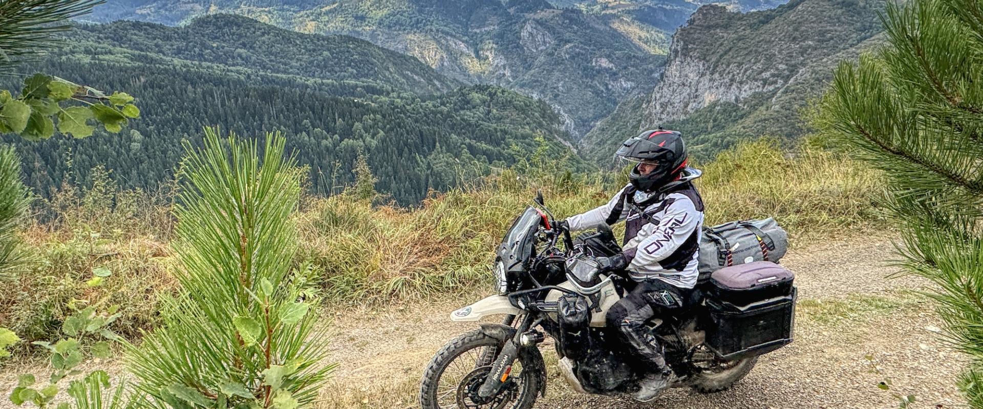 Motorradfahrer auf Bergpfad mit weitem, bewaldetem Tal im Hintergrund.