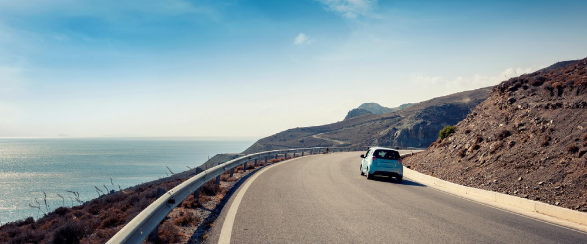 Kleines blaues Auto fährt auf Küstenstraße am Meer entlang