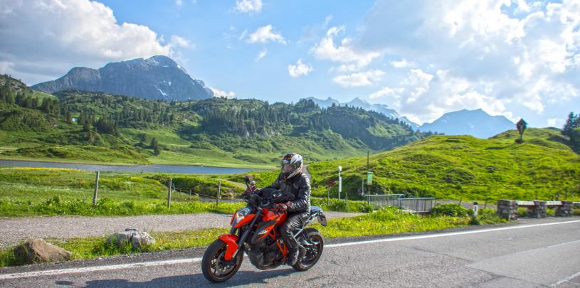 Motorradfahrer auf dem Hochtannbergpass, mit See, grünen Wiesen und Bergen im Hintergrund