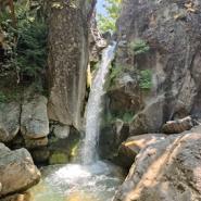 Ein natürlicher Wasserfall auf einer Motorradtour durch Griechenland fließt durch eine felsige Schlucht, umgeben von grüner Vegetation