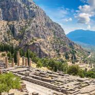 Antike Ruinen des Apollon-Tempels in Delphi, vor einer Bergkulisse und Blick ins Tal, unter einem teilweise bewölkten Himmel.