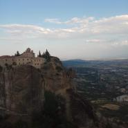 Ein Kloster thront auf einer steilen Felsklippe in Meteora, mit weitläufiger Aussicht auf die Ebene im Dämmerlicht