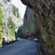 Eine Straße durch Bicaz Canyon mit einer Felsenschlucht mit steilen Wänden, Fahrzeuge parken rechts an der Straße, es laufen Menschen am Straßenrand 