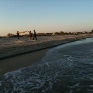 Schwarzes Meer am Strand sind 3 Personen bei Sonnenuntergang und mit sanften Wellen am Ufer